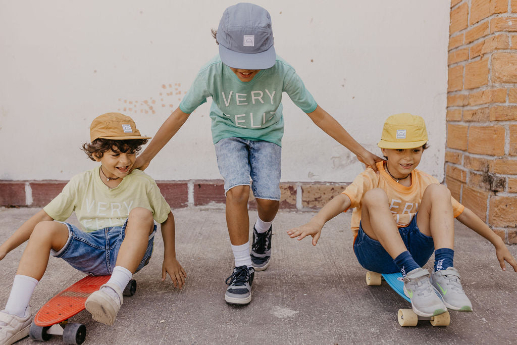 A family of four wearing Hey August Co caps and beanies, laughing together indoors