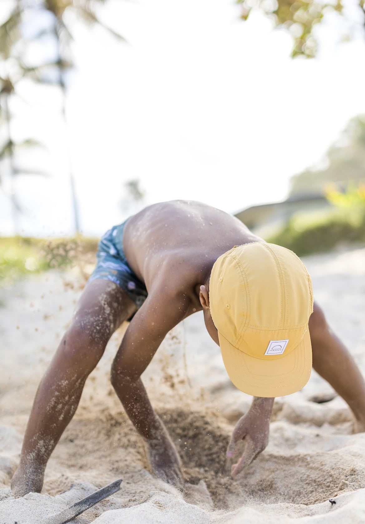 Kid wearing a Hey August cap on the beach giving a thumbs up
